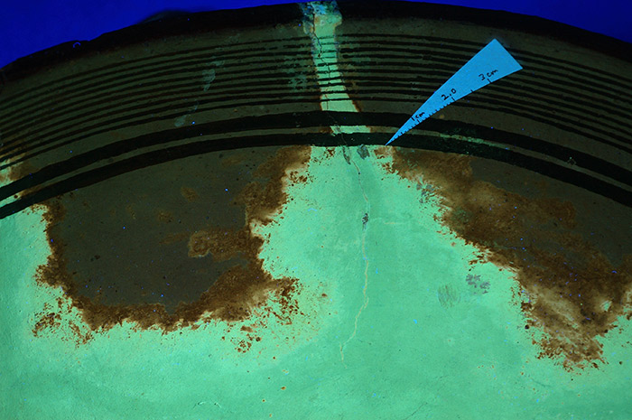 Ultra-violet light reveals the extent of leaching and staining on the clay body of the pot as a result of old restoration materials of a type no longer used today.